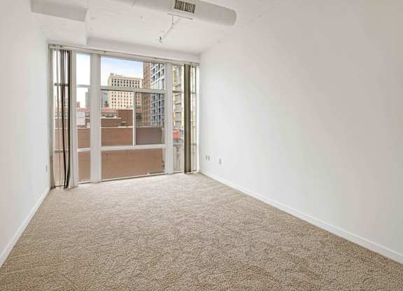 A room with a carpet floor and a window with a view of the city.