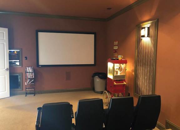 A home theater with a large screen and black chairs at The Legends at Steeplechase Apartments, Kentucky, 41094