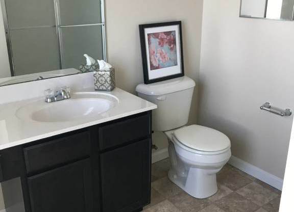 A bathroom with a white toilet, a sink with a black cabinet, and a framed picture on the wall at The Legends at Steeplechase Apartments, Richwood, Kentucky