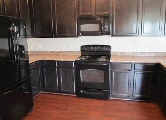 A black oven sits in a kitchen with wooden floors and dark brown cabinets at The Legends at Steeplechase Apartments, Kentucky