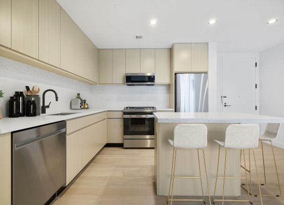 a kitchen with white cabinets and a island with three stools at The Paxton, Brooklyn, NY 11201