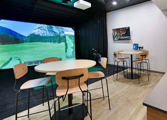 A room with a table, chairs, and a large screen displaying a mountainous landscape.