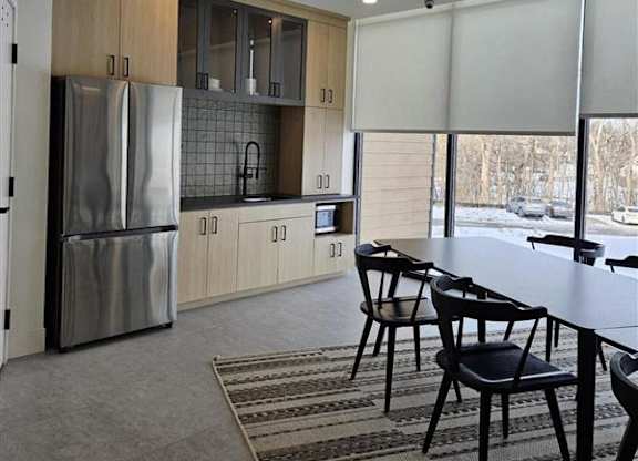 A kitchen with a refrigerator, cabinets, and a dining table.