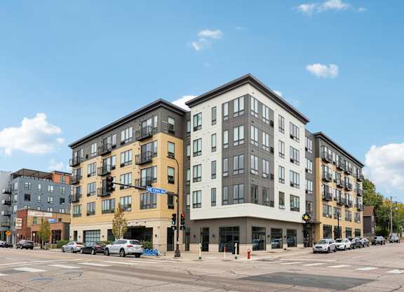 A street view of a multi-story building with cars parked in front.