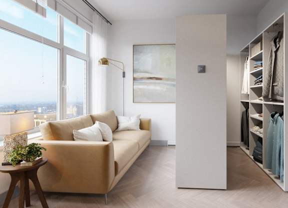 A room with a tan couch, a wooden table, and a large window overlooking the city.