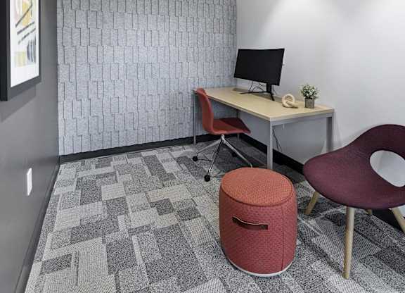 A small office with a desk, chair, and trash can.