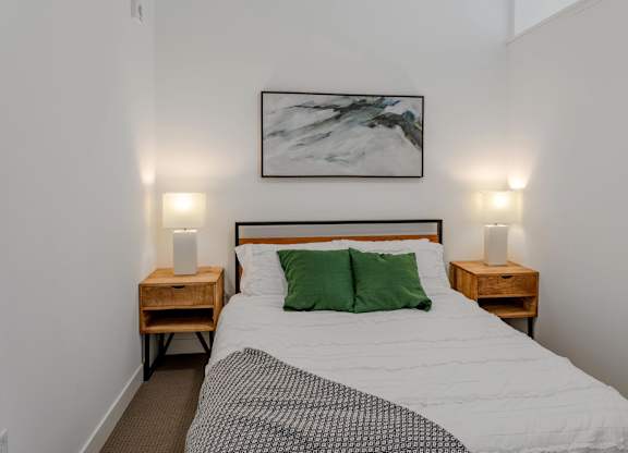 a bedroom with a bed with green pillows and a painting on the wall