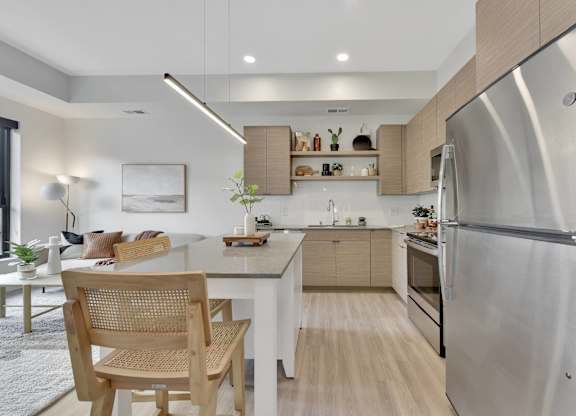 A modern kitchen with a stainless steel refrigerator and wooden chairs.