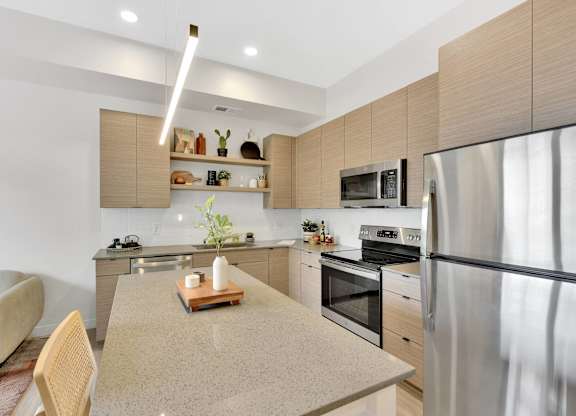 A modern kitchen with a stainless steel refrigerator, a wooden cutting board on the island, and a white chair.