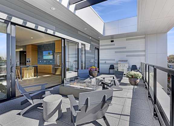 A modern balcony with grey furniture and a glass door leading to a living room.