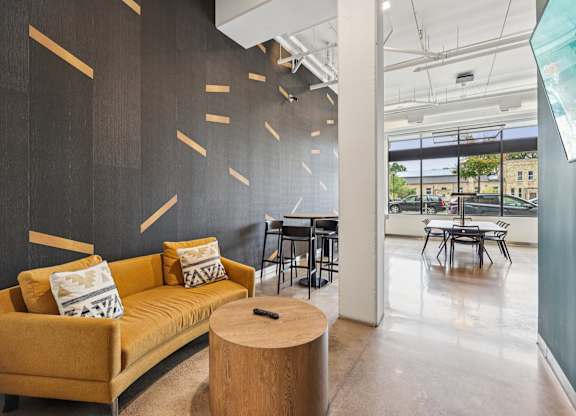 A yellow couch with a wooden coffee table in front of a black wall with wooden slats.