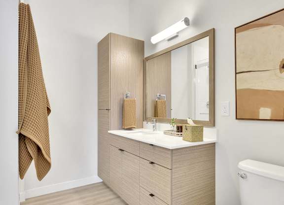 A white toilet sits in a bathroom with a wooden vanity and a mirror.