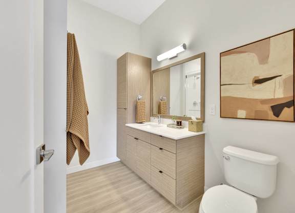 A bathroom with a white toilet, a wooden vanity with a mirror, and a brown towel hanging on the door.