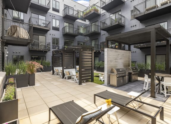 a patio with tables and chairs and a grill in front of an apartment building