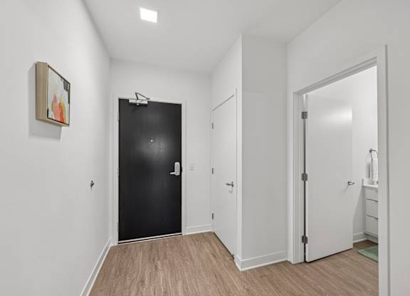 A black door is in a white room with a wooden floor.