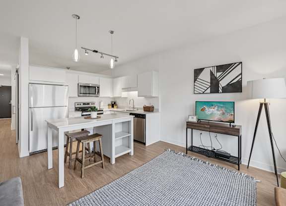 A modern kitchen with white appliances and a dining area with a grey rug.