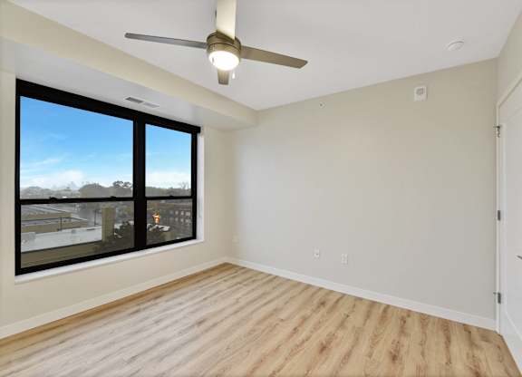 A room with a ceiling fan and a large window overlooking a cityscape.