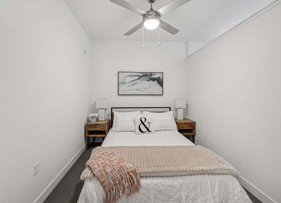 A bedroom with a bed, a ceiling fan, and a painting on the wall.
