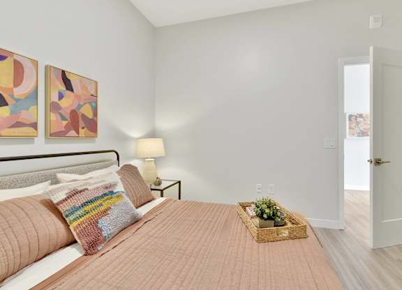 A bedroom with a bed, two lamps, a basket of flowers, and two paintings on the wall.