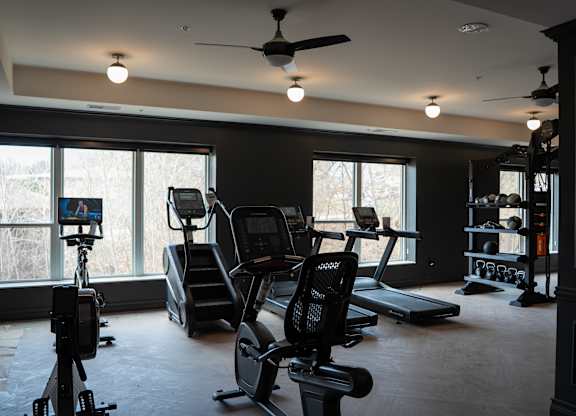 A home gym with treadmills, elliptical machines, and a fan.