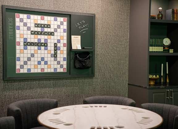 A Scrabble board is on the wall above a table.