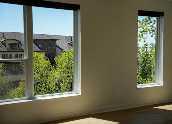 Two windows in a room with a view of houses and trees outside.