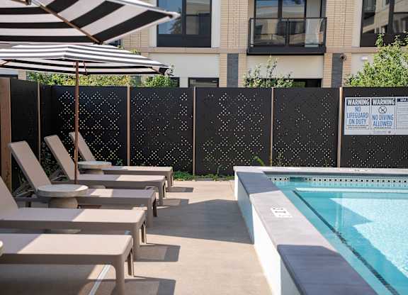 A pool area with sun loungers and a black and white striped umbrella.
