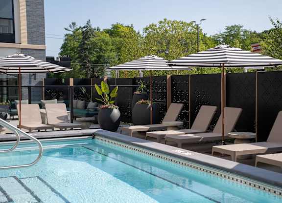 A pool with chairs and umbrellas is surrounded by a black fence.