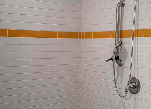 A white tiled shower with a black drain.