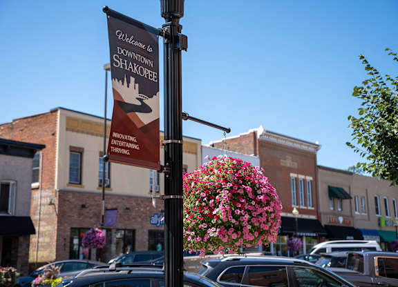 A sign welcoming people to Downtown Shakopee hangs on a pole.
