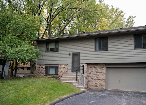 A house with a grey siding and a black door is surrounded by trees.