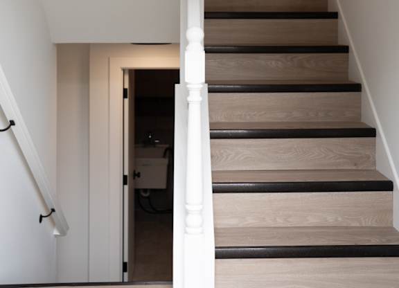 A staircase with a black railing leads to a kitchen area.