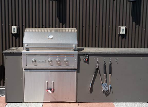 A stainless steel grill with utensils hanging on the wall.