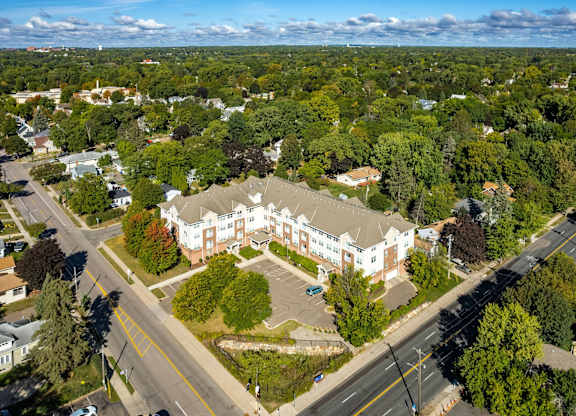 An aerial view of a large white building surrounded by trees and a road in front.