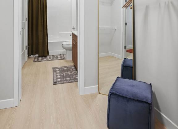 A room with a wooden floor and a white wall with a closet and a toilet.