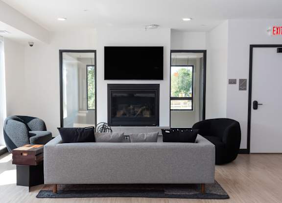 A modern living room with a grey couch, a black chair, a fireplace, and a flat screen TV mounted on the wall.