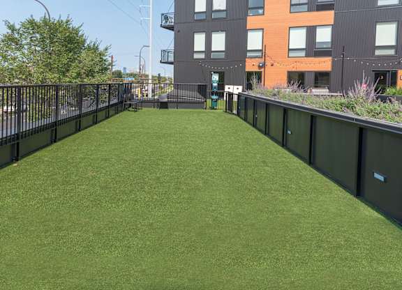 A grassy area in front of a building with a fence on the left side.
