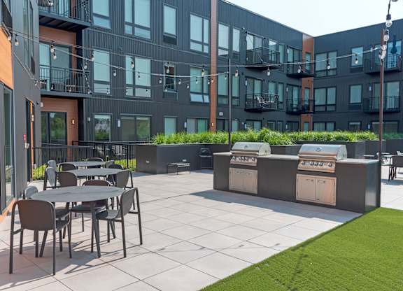 A patio with tables and chairs is surrounded by a black building.