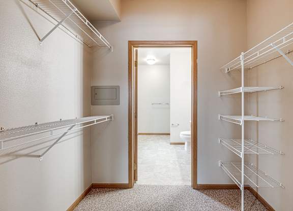 A walk-in closet with white shelving and a mirrored doorway.