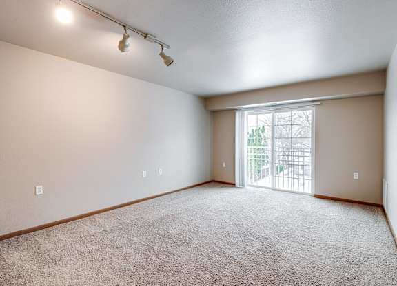 A room with a carpeted floor and a sliding glass door leading to a balcony.