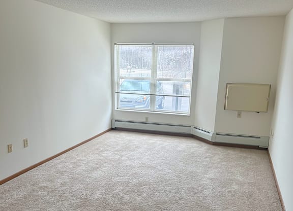 A carpeted room with a window and a wall-mounted TV.