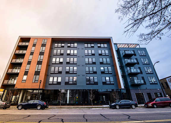 A modern multi-story apartment building with cars parked in front.