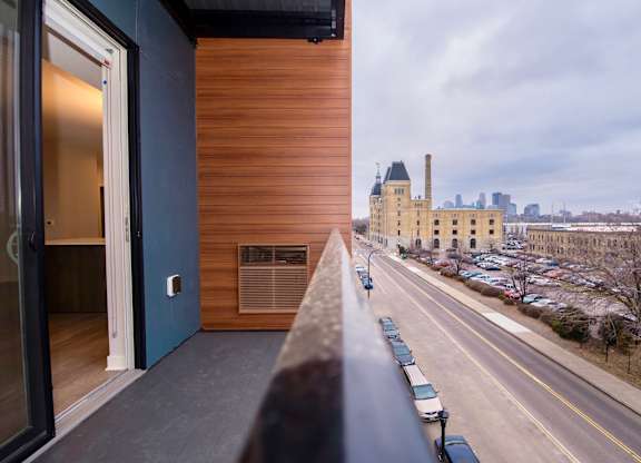 A view from a window of a building overlooking a street with cars and a building with a tower in the distance.