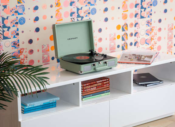 A record player sits on a shelf with books and a plant.