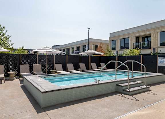A pool surrounded by a black fence and a few chairs.