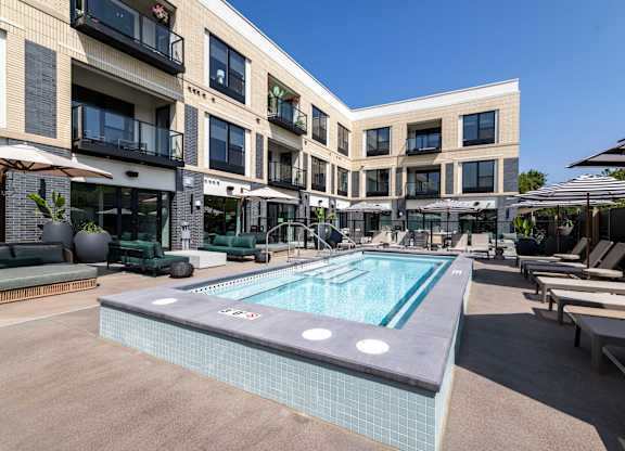 A swimming pool in the middle of a courtyard surrounded by lounge chairs and umbrellas.