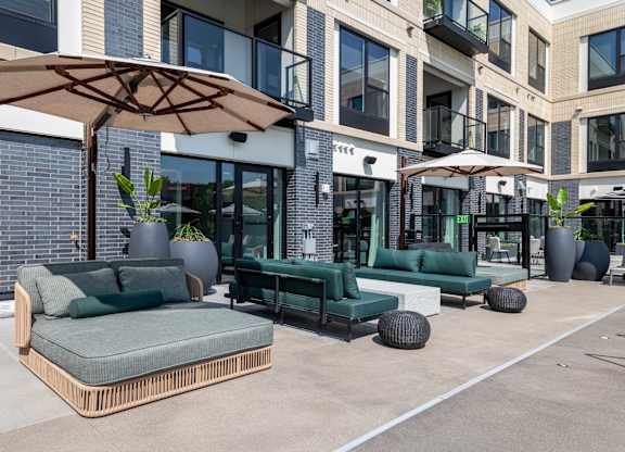 A patio with a green couch and a brown umbrella.