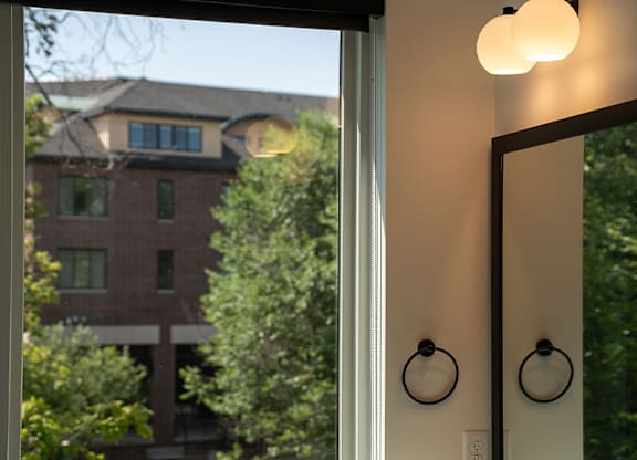 A bathroom with a large mirror and a window overlooking a street.