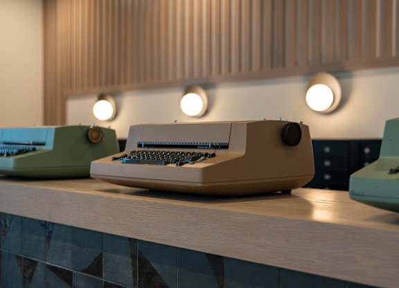 A vintage typewriter is placed on a desk with a blue typewriter to its left and a green typewriter to its right.