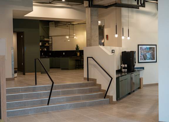 A staircase with a black railing leads to a kitchen area.